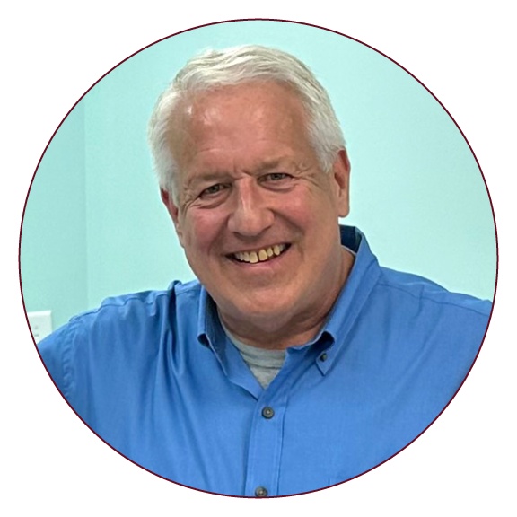 A photo of a man with white hair wearing a blue shirt in a sea-green room.